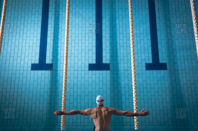 High angle view of a male Caucasian swimmer wearing a white swimming cap diving in the swimming pool