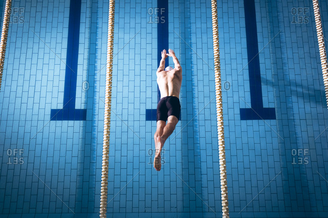High angle view of a male Caucasian swimmer wearing a white swimming cap diving in the swimming pool