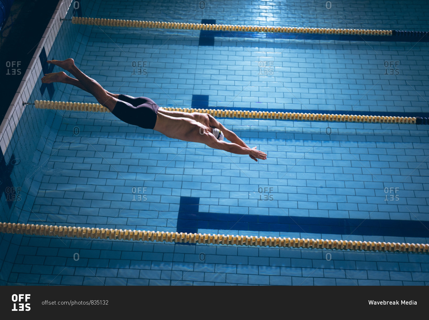 High angle view of a male Caucasian swimmer wearing a white swimming cap diving in the swimming pool