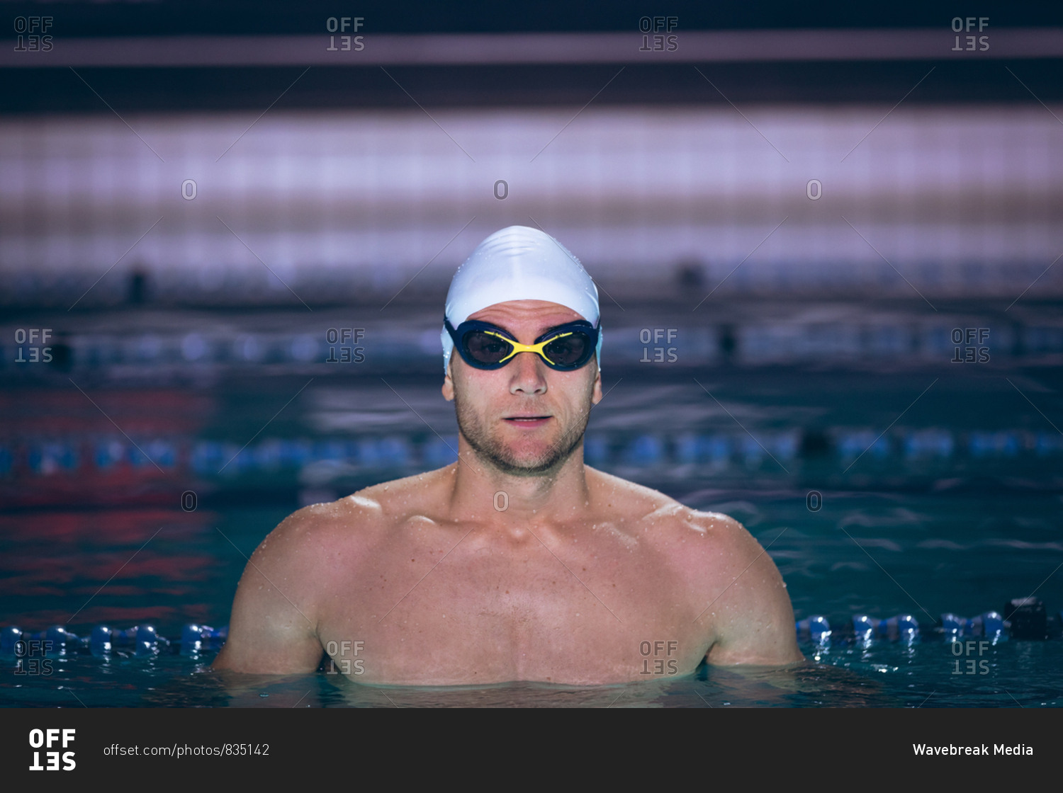 Front view of a male Caucasian swimmer wearing a white swimming cap and goggles while standing in the swimming pool