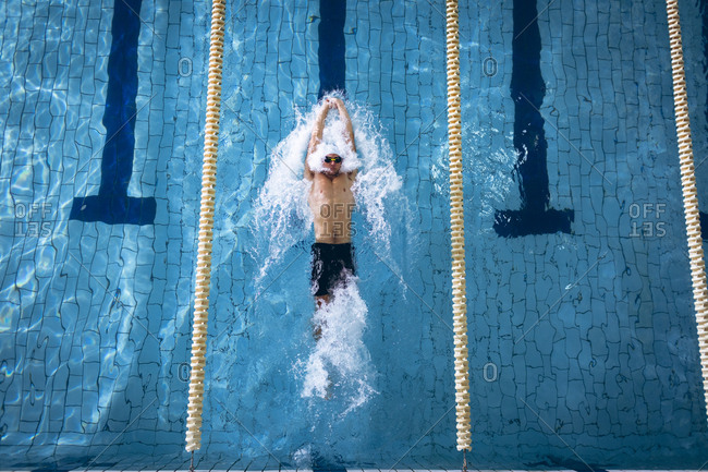 High angle view of a male Caucasian swimmer wearing a white swimming cap and goggles doing a back stroke in the swimming pool