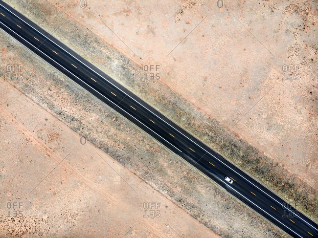 Aerial view of a paved road with a slight curve passing in the middle of a  desert land. The roadway has one lane for each direction of travel. Stock  Photo