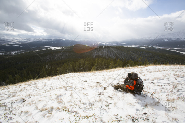 A male hunter looks through binoculars in the snow.