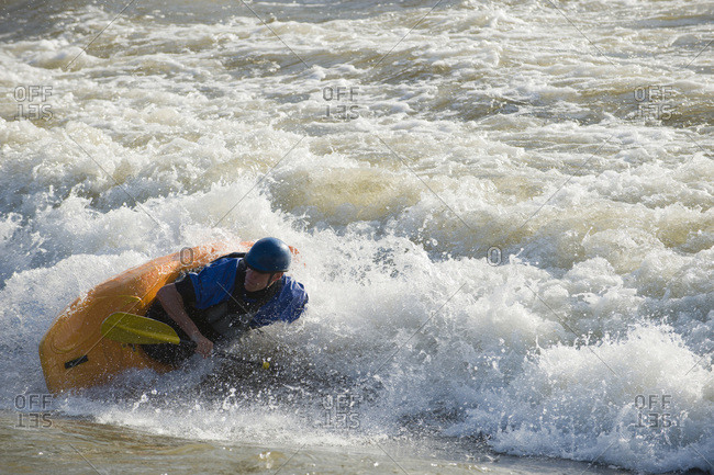 A male whitewater kayaker plays on the Missoula playwave.