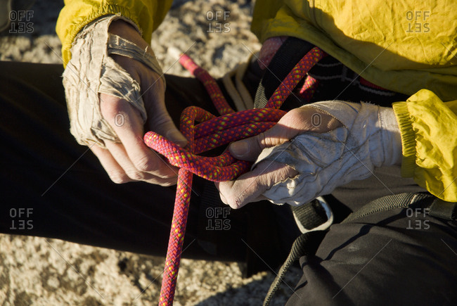 The weathered hands of a climber tie into a harness.