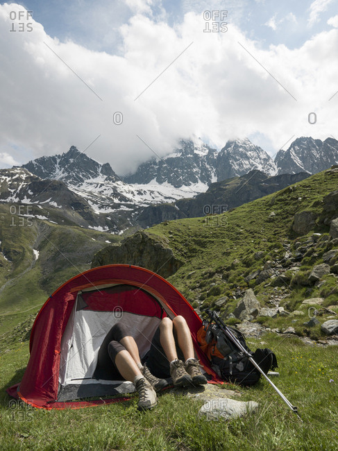 Hikers' legs protrude from tent in alpine meadow, mountains