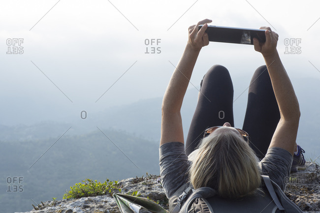 Mature woman hiker reclines on cliff edge with pad