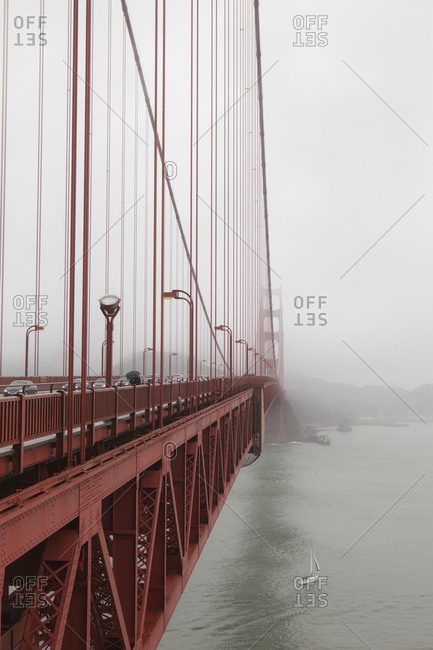 A small sailboat passes under the Golden Gate Bridge on a foggy day in San Francisco, California.