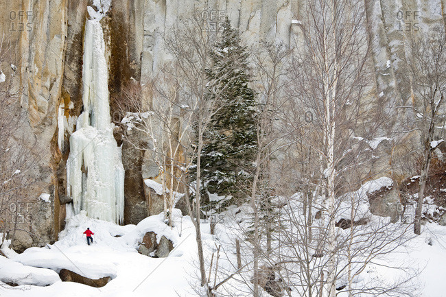 A man is standing at the base of a frozen waterfall in Sounkyo Gorge, Daisetsuzan National Park, Hokkaido, Japan.
