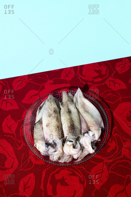 Some raw cuttlefishes in a glass plate, placed on a red flower-patterned tablecloth