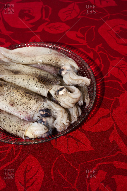 Closeup of some raw cuttlefishes in a glass plate, placed on a red flower-patterned tablecloth