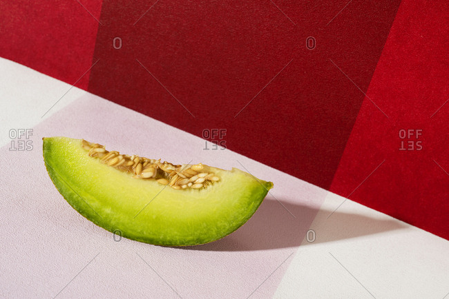 Closeup of a slice of galia melon on a white and red background
