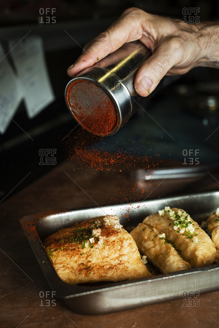 Closeup of a caucasian man sprinkling paprika on some battered and fried pieces of codfish