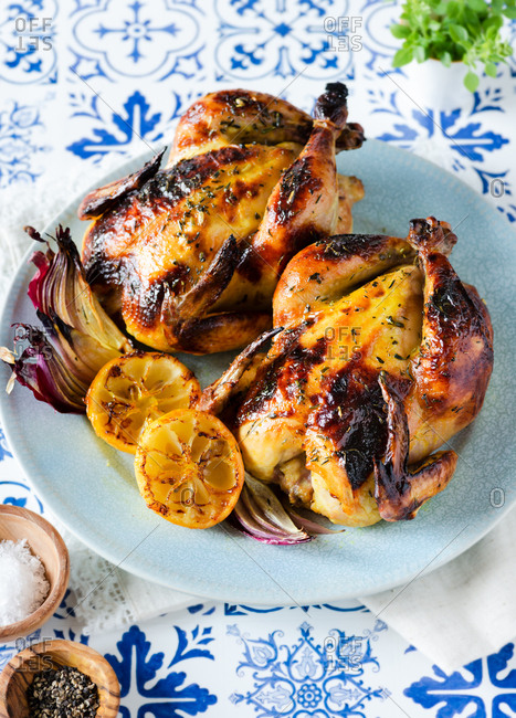 Roasted chickens cornish hens with lemon and onions on blue plate over blue tile background