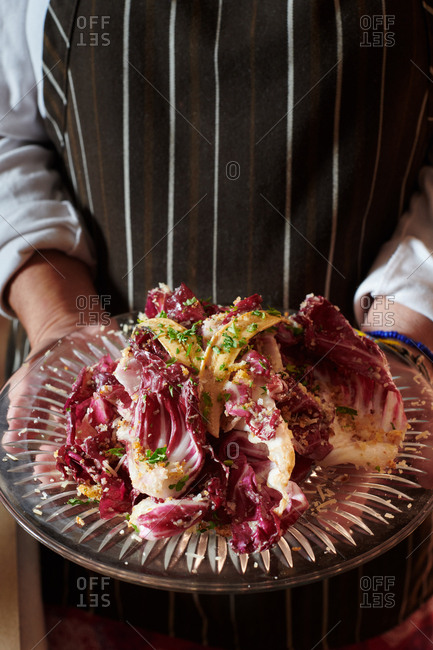 Radicchio Bacon and Anchovy knife and fork salad held by a chef in a restaurant wearing an apron.
