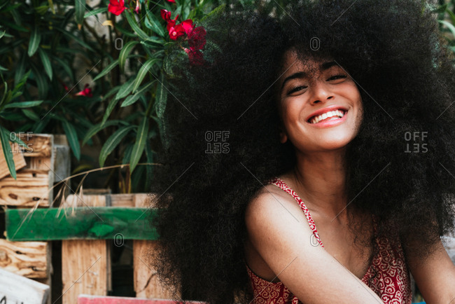 Portrait of a girl with curly hair and big smile seated outdoor, wearing a comfy dress. she is looking at the camera and smiling