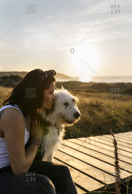 Woman cuddling with dog on boardwalk in dunes