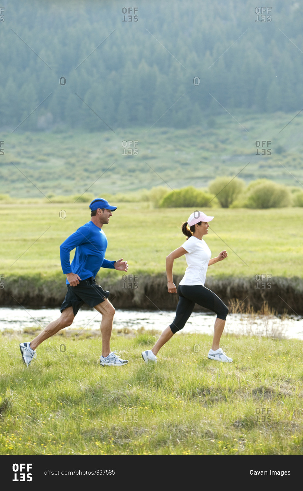 An athletic couple trail running through a field next to a river.