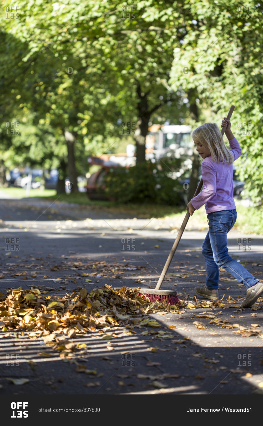 Girl sweeping leaves on pavement
