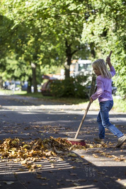 Girl sweeping leaves on pavement