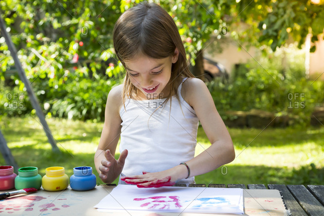 Smiling little girl printing color on sheet of paper with her hand