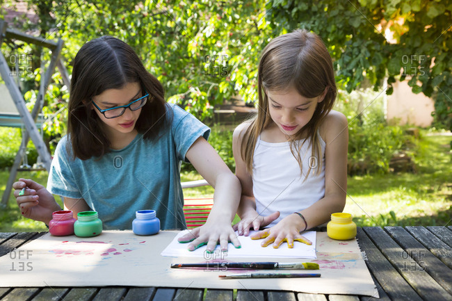 Sisters printing color on sheet of paper with their hands