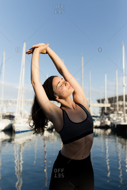 Front view of young woman doing stretching exercises in front of port of Barcelona