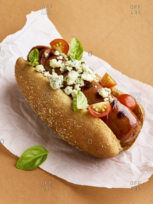Hot dog topped with tomatoes, blue cheese, and basil