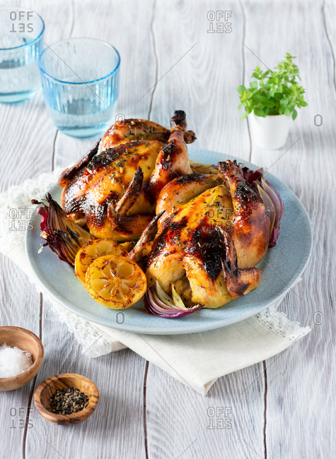 Homemade roasted cornish hens with lemon and onions on blue plate over wooden background