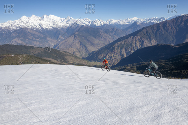 Gosainkund, Nepal - March 28, 2019: Mountain bikers descend a snow covered slope in the Himalayas with views of the Langtang range in the distance