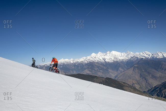 Gosainkund, Nepal - March 28, 2019: Mountain bikers cycle along a snow covered slope in the Himalayas with views of the Langtang range in the distance