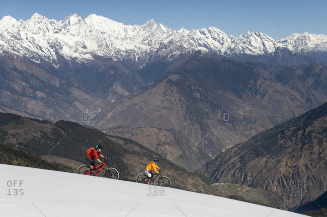 Gosainkund, Nepal - March 28, 2019: Mountain bikers on a snow covered slope in the Himalayas with views of the Langtang mountain range