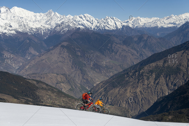 Gosainkund, Nepal - March 28, 2019: Men mountain biking on a snow covered slope in the Himalayas with views of the Langtang mountain range