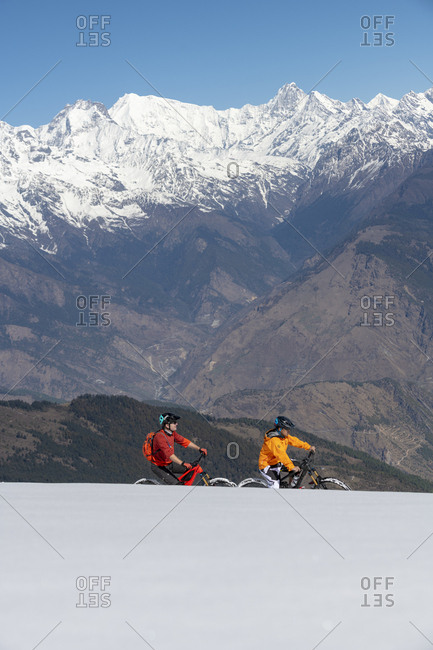 Gosainkund, Nepal - March 28, 2019: Two men mountain biking on a snow covered slope in the Himalayas with views of the Langtang mountain range