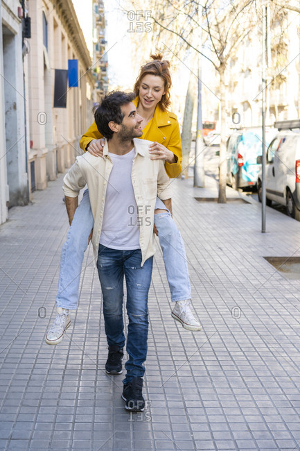 Man giving girlfriend a piggyback ride on pavement in the city