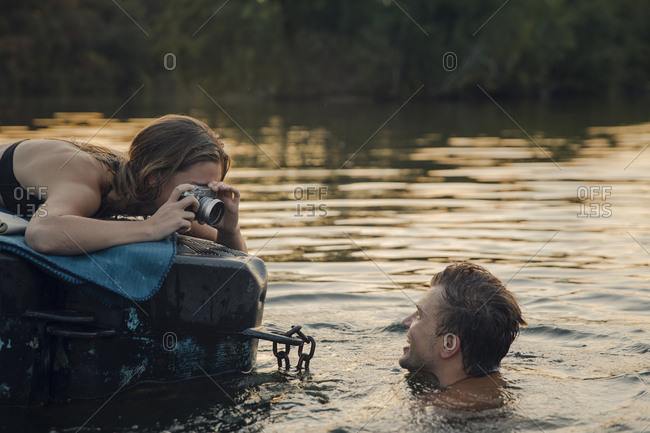 Young woman lying on bathing platform- taking pictures of a laughing young man