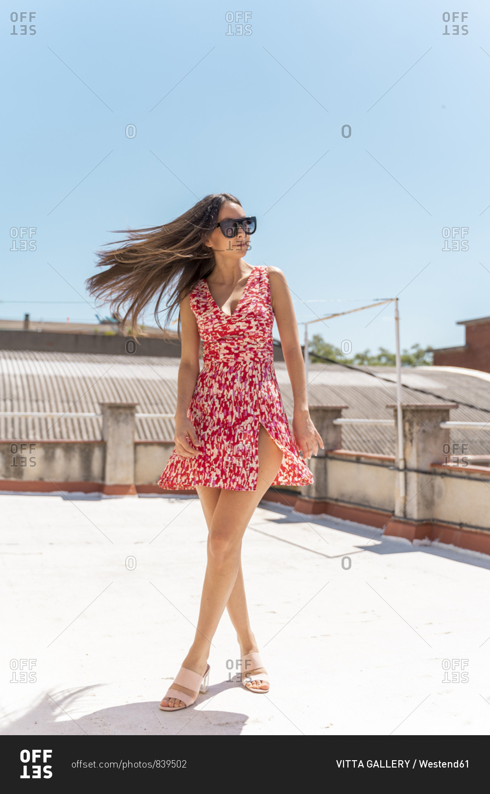 Portrait of young woman on roof top wearing fashionable summer dress tossing her hair