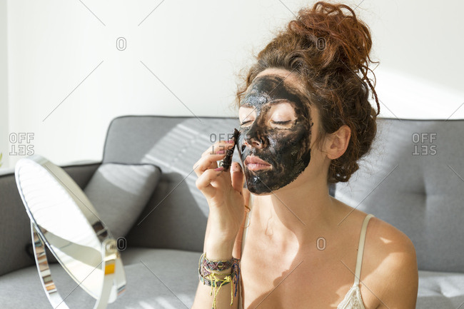 Young woman applying facial mask at home
