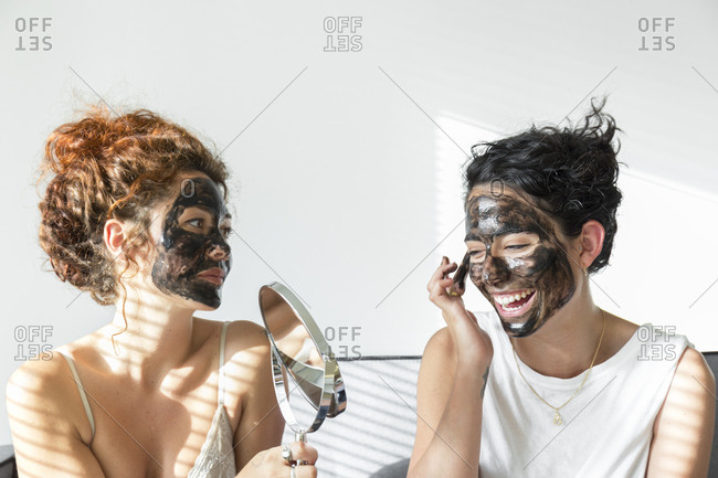 Two happy young women applying facial masks at home