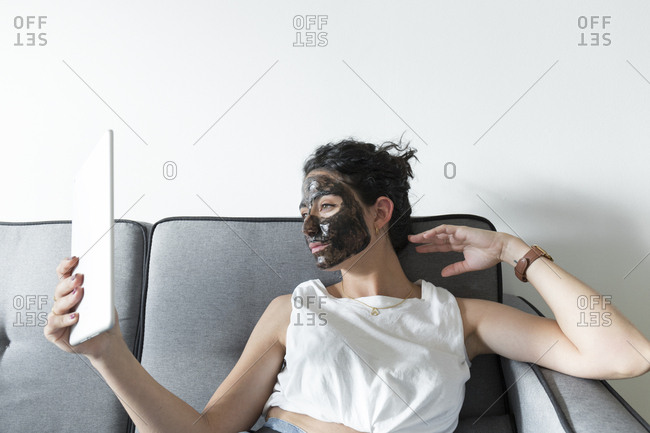 Young woman wearing facial mask and using tablet at home