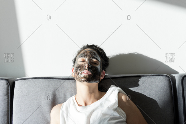 Relaxed young woman wearing facial mask at home