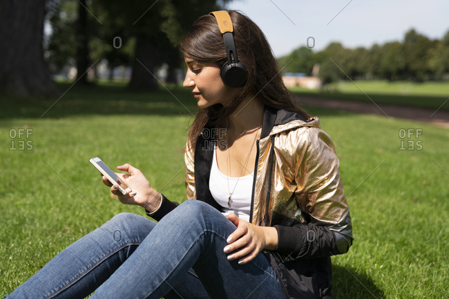 Portrait of young woman wearing shiny jacket and using smartphone and headphones