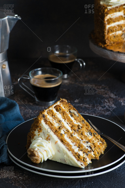Slice of carrot cake with walnuts on black plate served with coffee