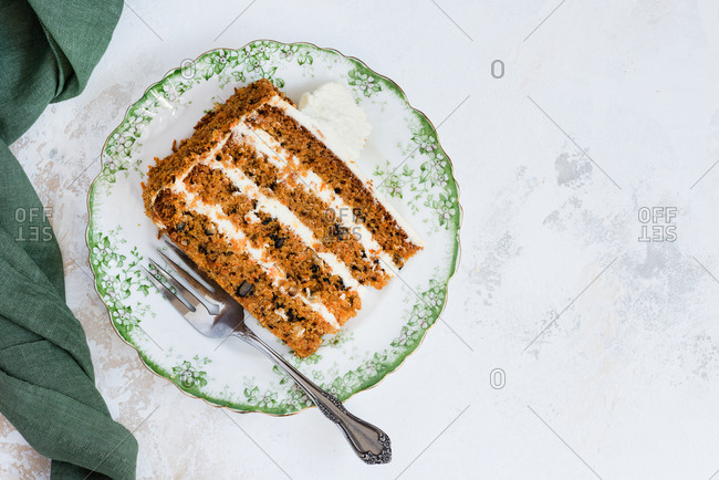 Slice of carrot cake with walnuts on a plate against a light background