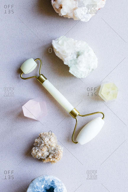 Flatlay of jade facial roller surrounded by crystals and gemstones