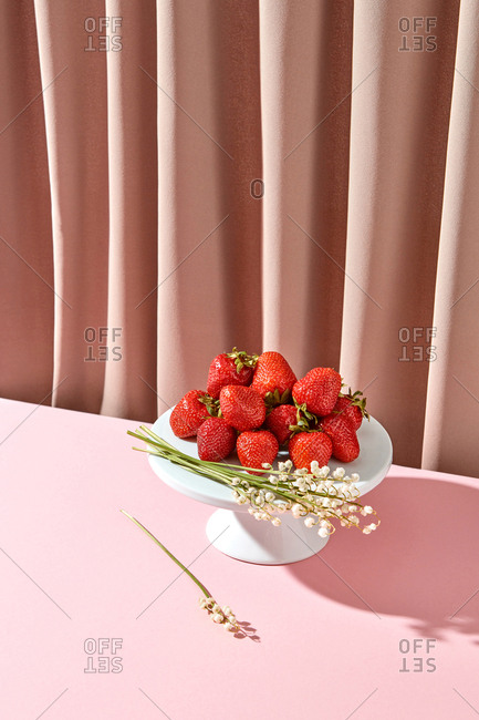 Freshly picked organic strawberries and spring flowers on a ceramic cake stand