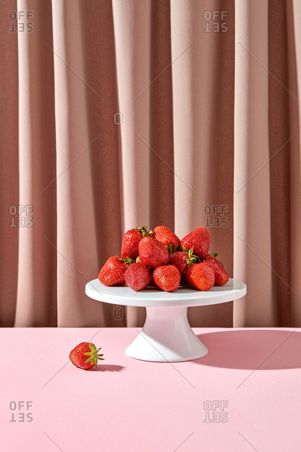 Organic freshly picked strawberries on a plate with shadow on a textile draped background.