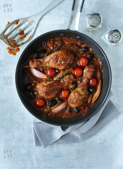 Mediterranean chicken legs with ingredients and sauce in a pan with a cruet