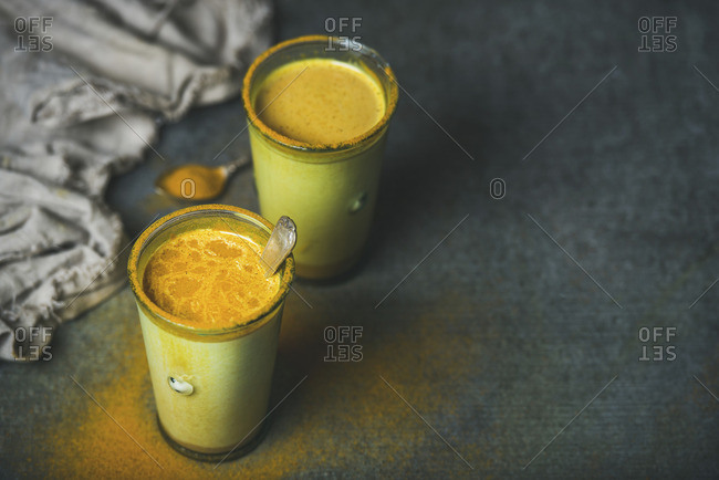 Golden milk with turmeric powder in glasses over dark grunge background