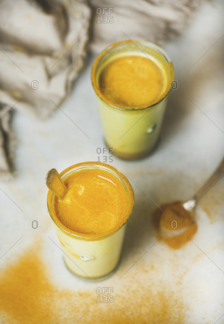 Golden milk with turmeric powder in glasses over grey marble background
